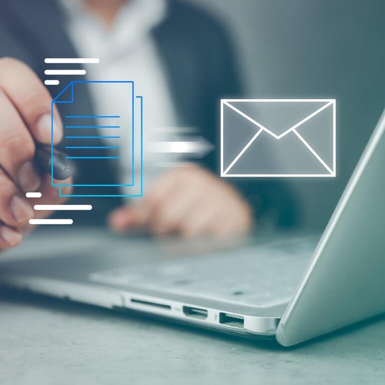 A person with a laptop dragging a file into an email.